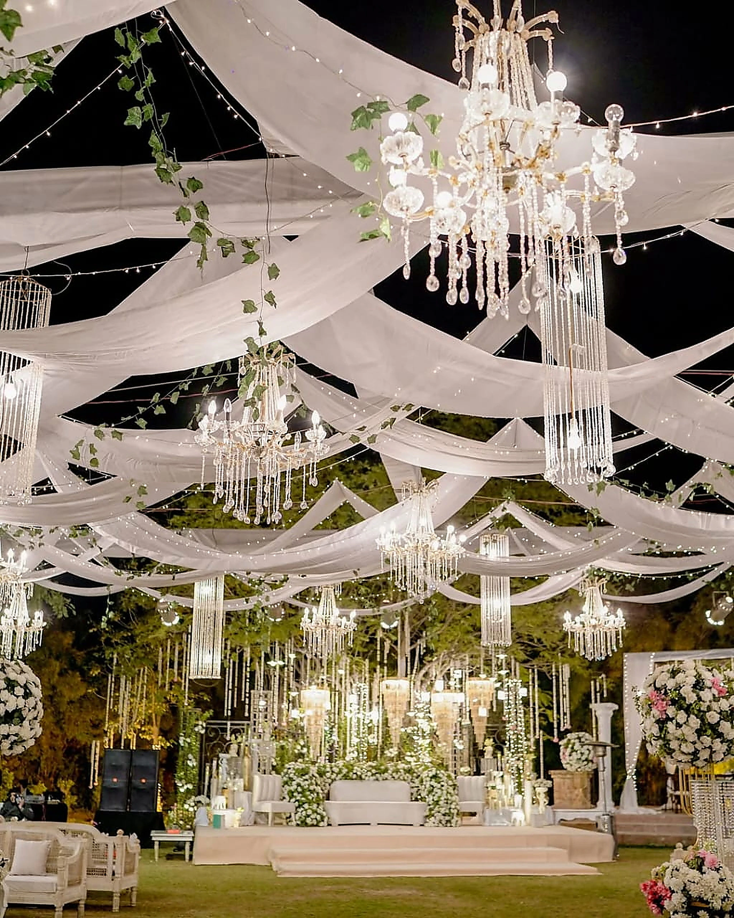 Draped white ceiling and layered chandeliers above a walima stage
